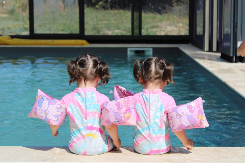 Deux petites filles de dos au bord d’une piscine, brassards roses.