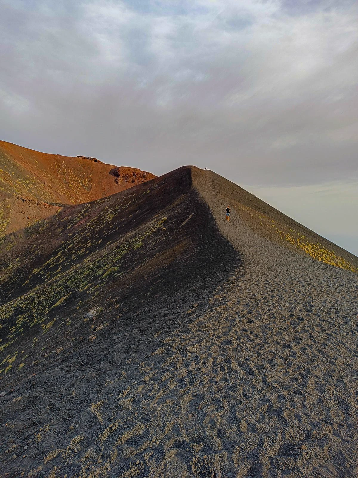 Crête volcanique de l’Etna au crépuscule, une silhouette minuscule marche sur l’arête de cendre.