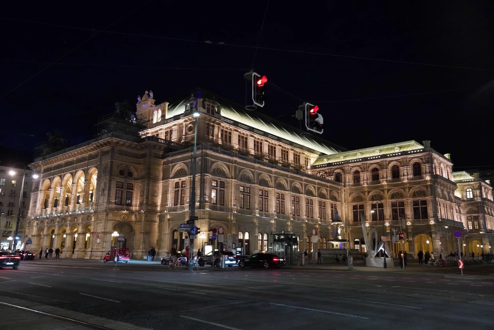 L’Opéra de Vienne illuminé la nuit à l’angle d’un boulevard, feux rouges suspendus au premier plan.