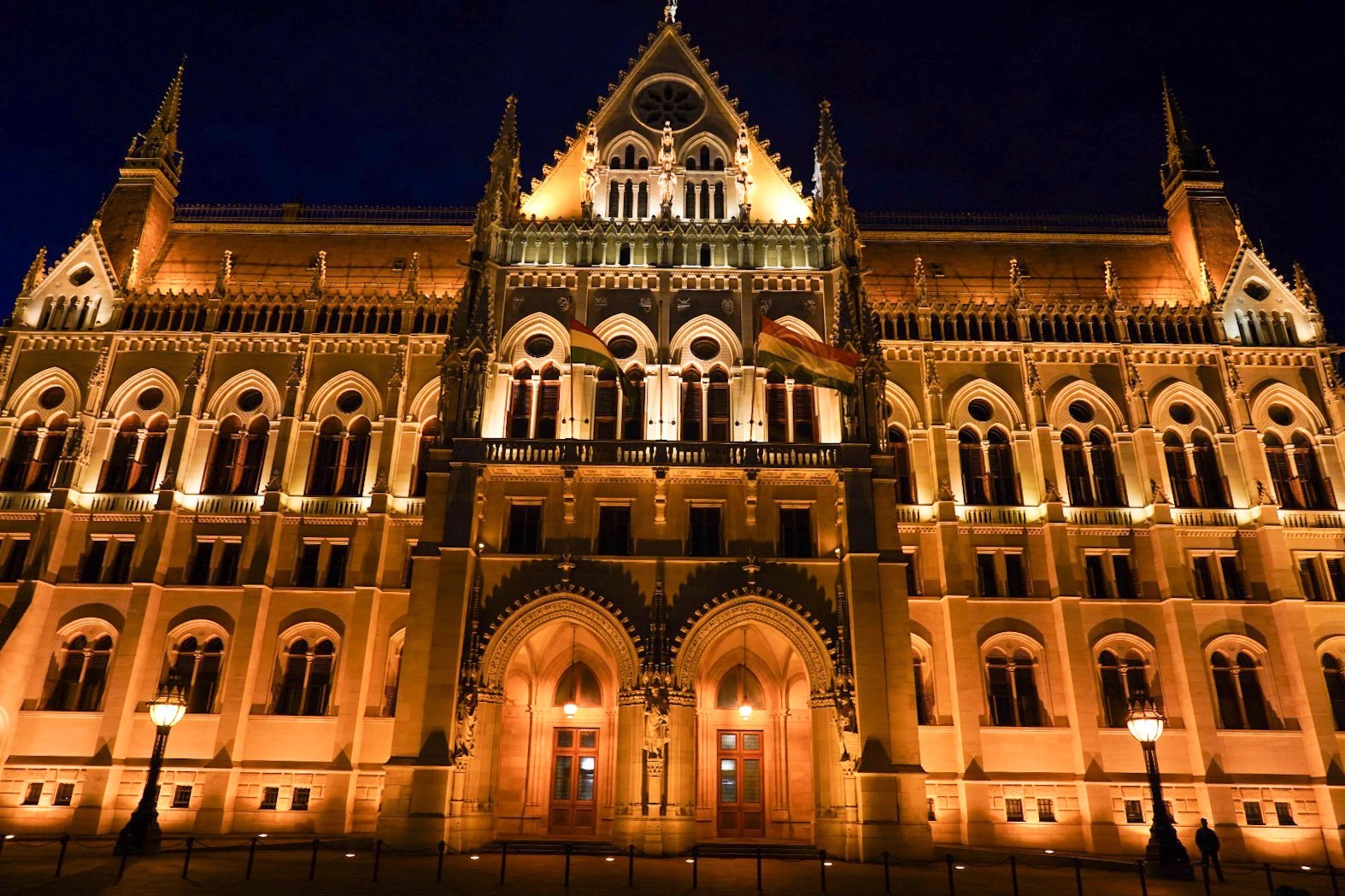 Façade néogothique du Parlement de Budapest illuminée en or contre un ciel bleu nuit.
