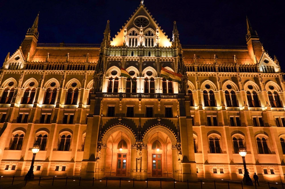 Façade du Parlement de Budapest illuminée en or la nuit.